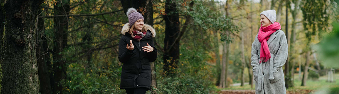 Zwei Frauen in Winterkleidung spazieren zusammen durch den Wald und unterhalten sich