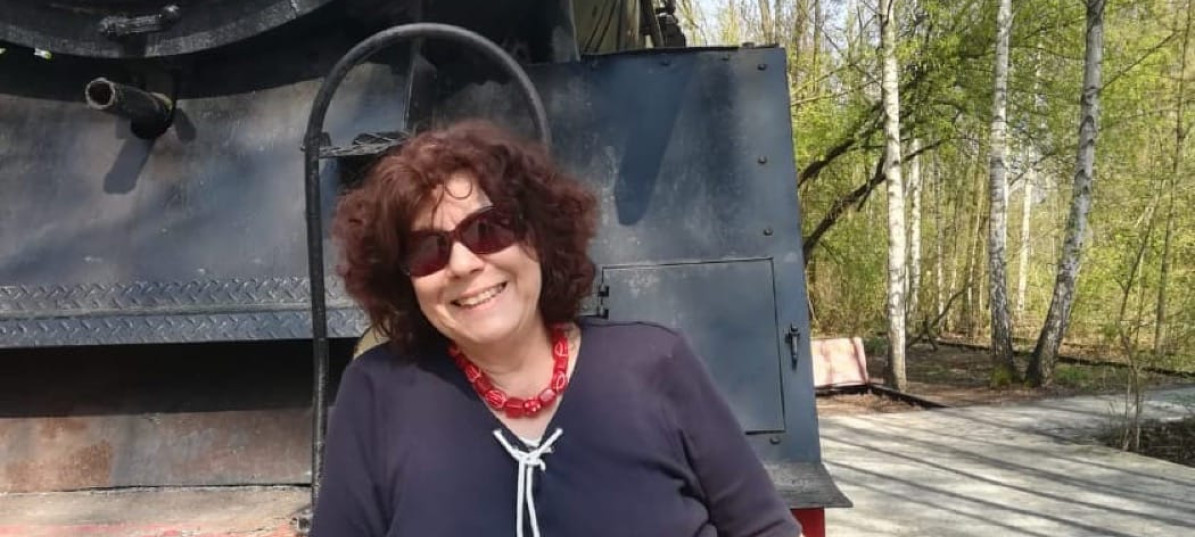 Renate steht im Freizeitoutfit vor einer alten Dampflok und lächelt in die Kamera