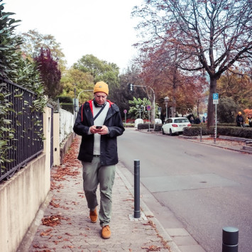 Mann mit gelber Mütze läuft auf Bürgersteig und schaut auf sein Handy.