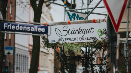 Neben dem Straßenschild der Friedensallee in Hamburg hängt das Ladenschild von Stückgut. In geschwungenen Buchstaben steht dort 